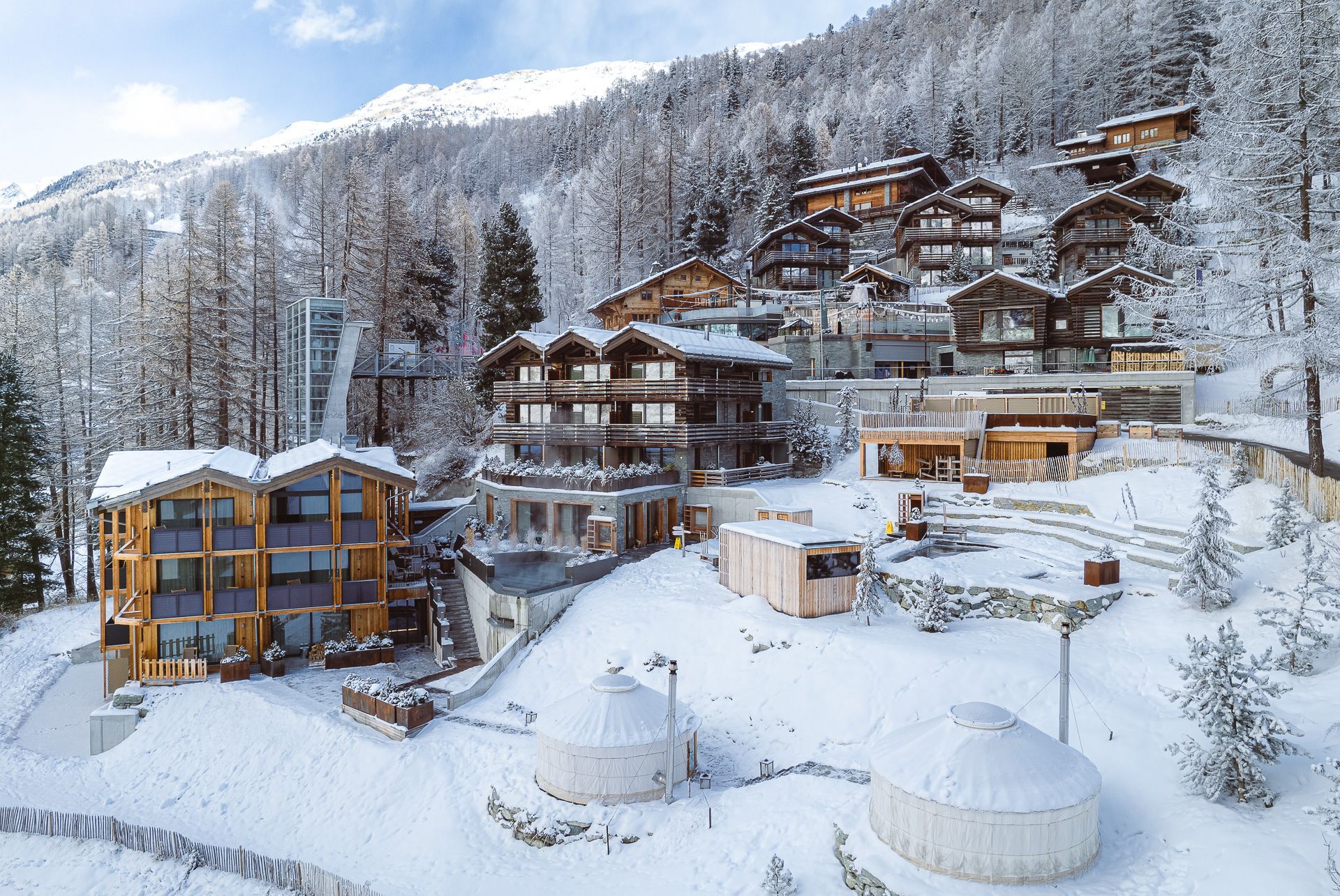 Snowy mountain resort with wooden buildings and yurt-like structures.