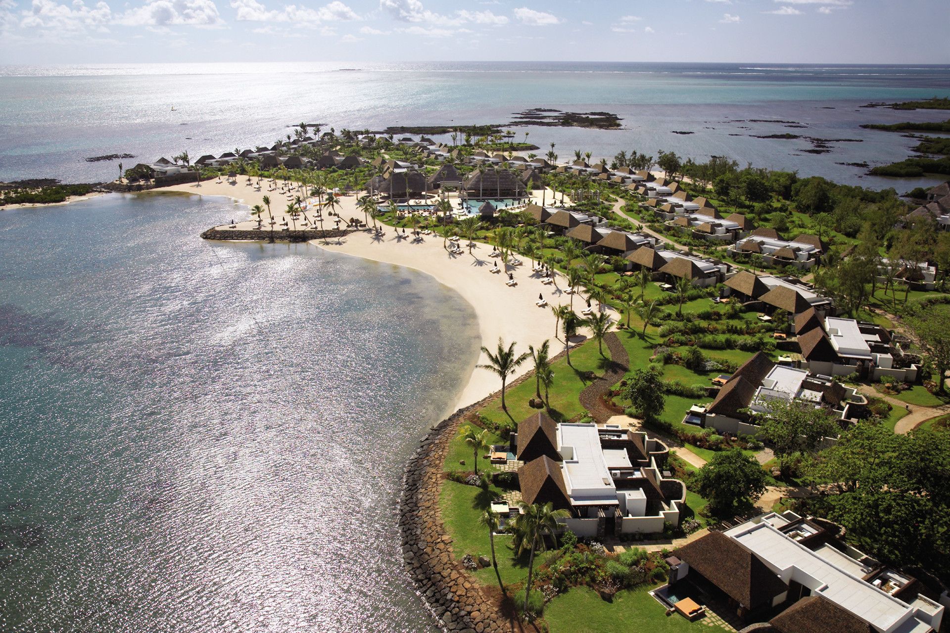 Aerial view of a Four Seasons at Anahita Mauritius with villas, palm trees, and turquoise water across a curved shoreline