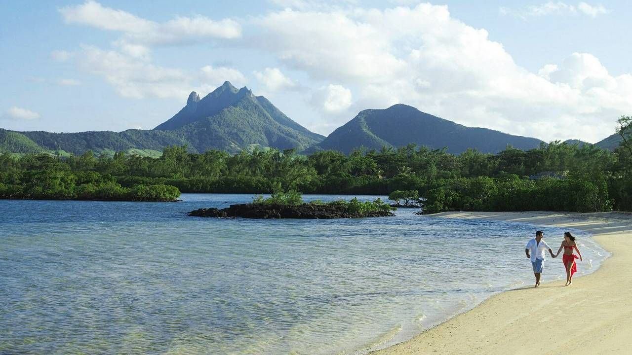 Tropical beach with blue water, lush green pitons, and two people walking along the shore