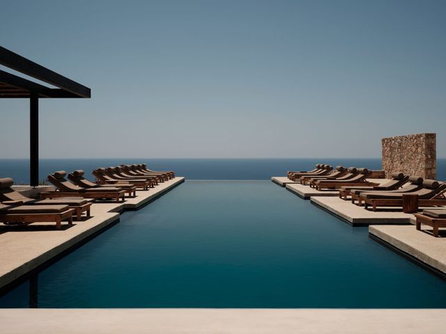 Infinity pool overlooking the ocean, flanked by rows of brown lounge chairs and a shaded patio.