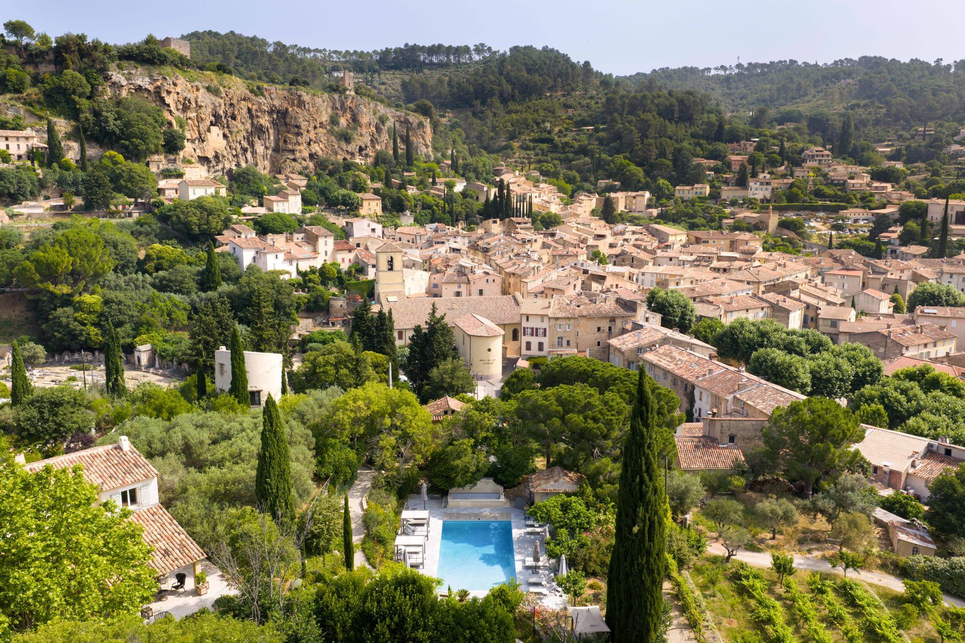 View of a French village nestled in a valley, with stone buildings, red-tiled roofs, and a pool.