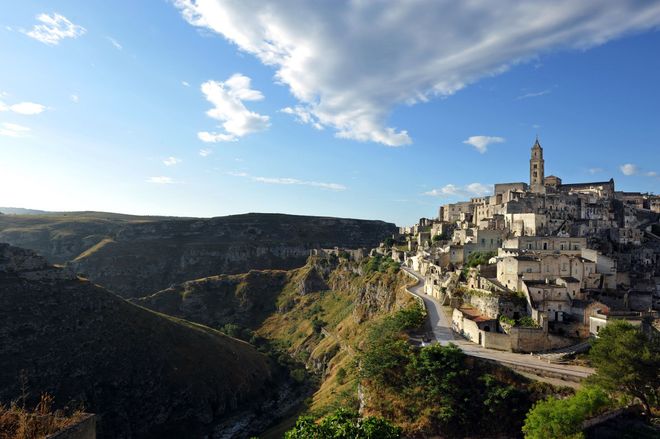 Italian hilltop village of stone buildings beside a deep canyon under a bright blue sky