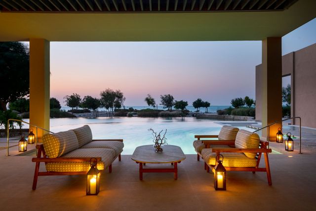 Poolside patio at sunset with lantern-lit seating overlooking an infinity pool and palm trees.