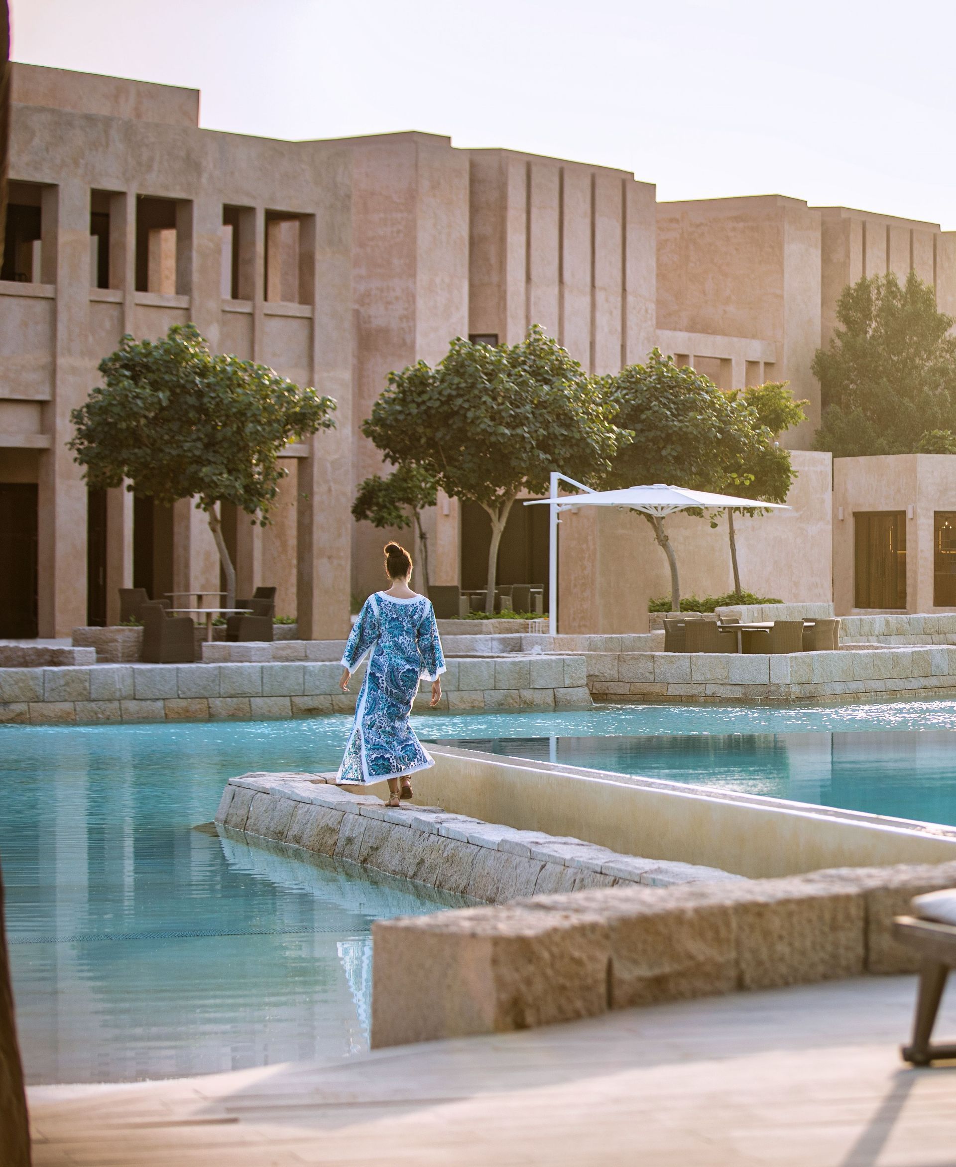 A woman in a blue dress is standing next to a pool in front of a building.