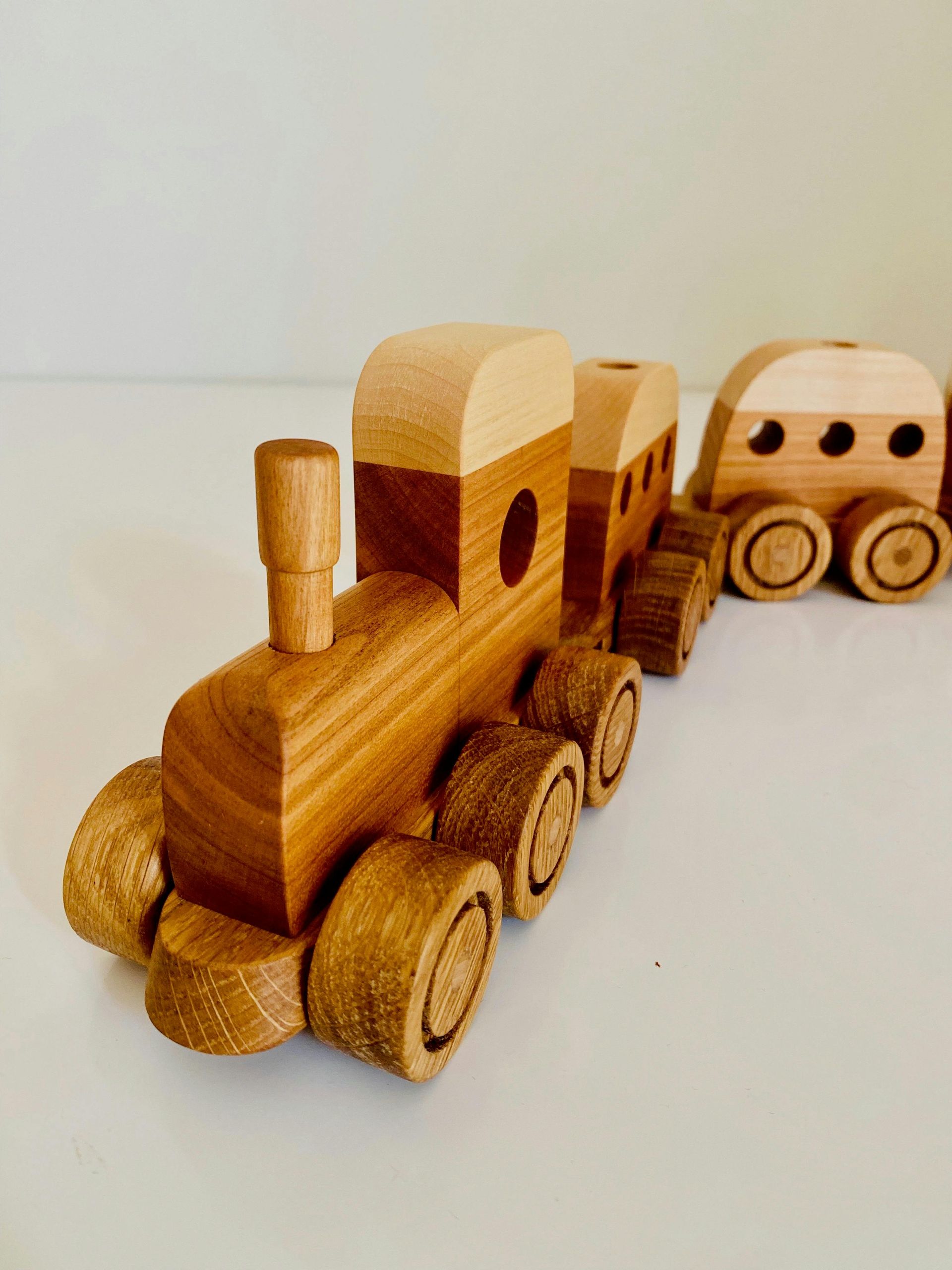 Wooden toy train and wagon on a light surface, with a small house-like car behind it.