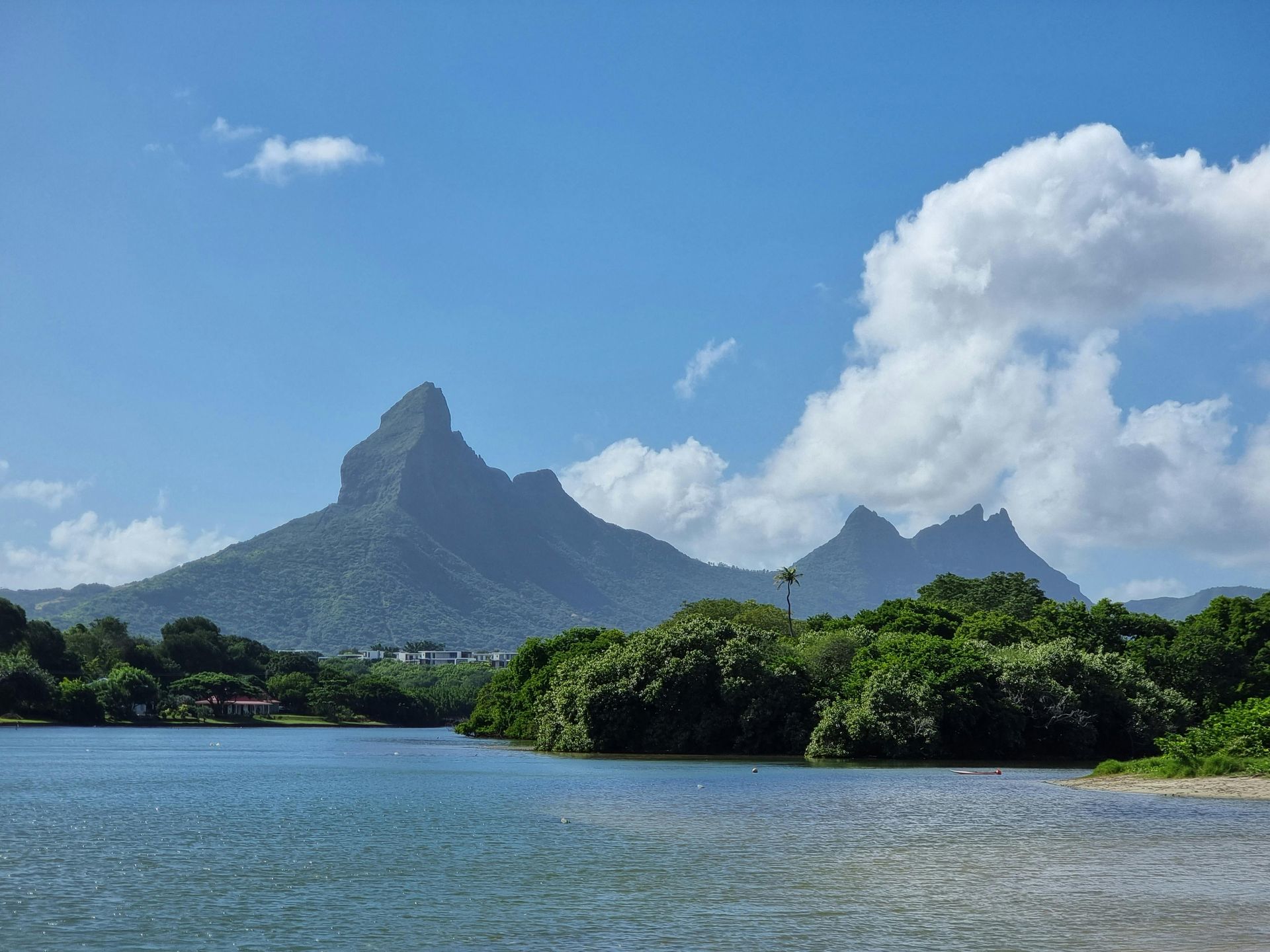 Tropical lagoon with blue water, green shoreline, and a Mauritian Piton mountain under cloudy sky