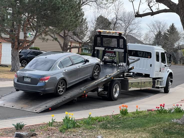 Tow truck loading a gray sedan on a residential street with spring flowers nearby