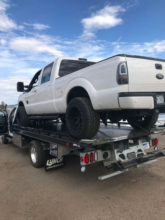 White lifted pickup truck on a flatbed tow truck under a blue sky