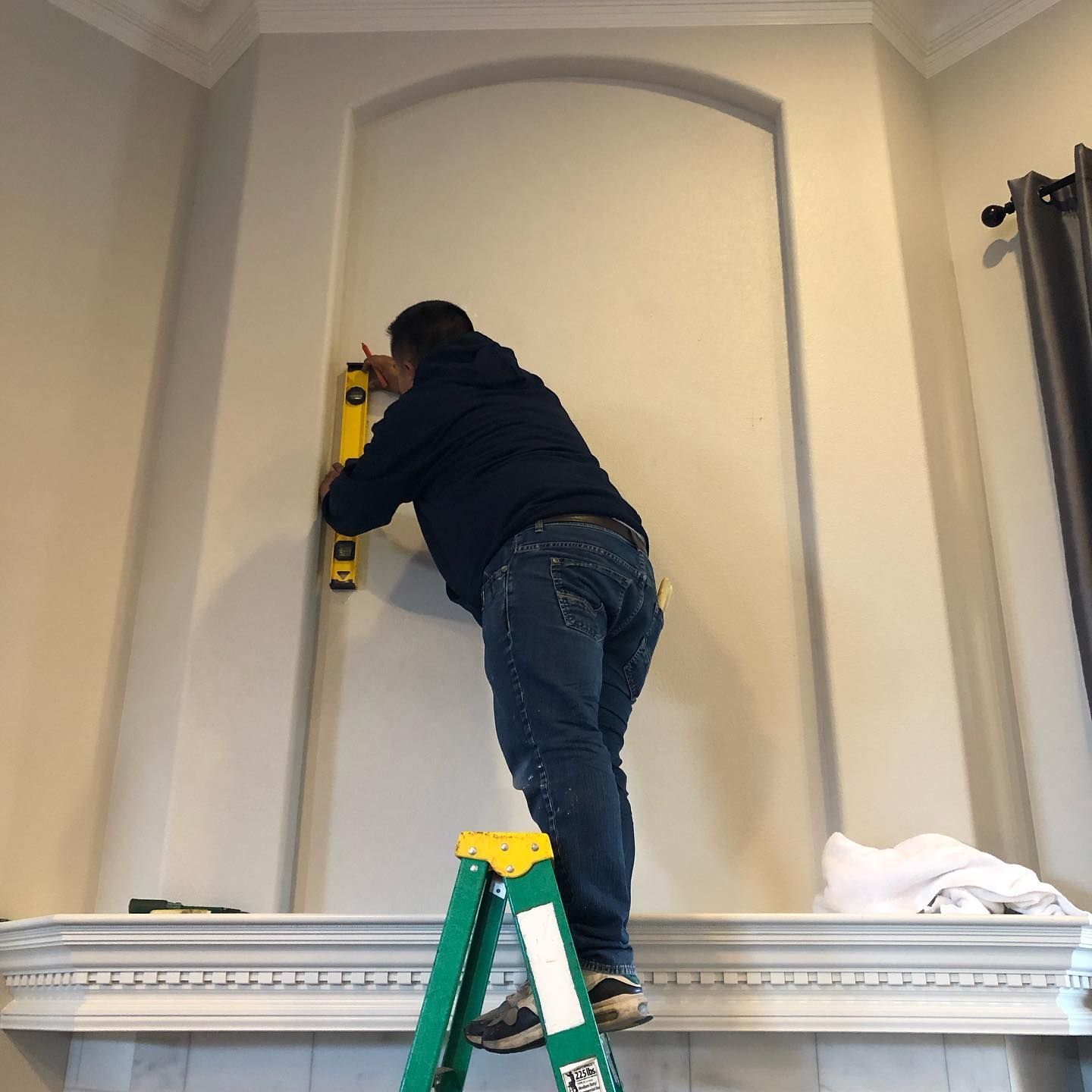 a man on a ladder measuring a wall with a yellow level