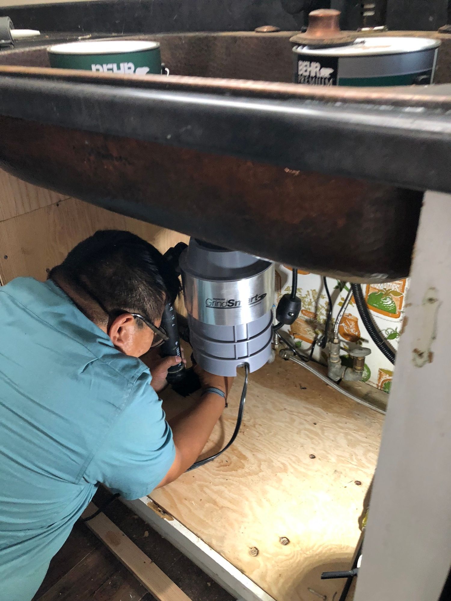 a man is working on a garbage disposal under a sink .