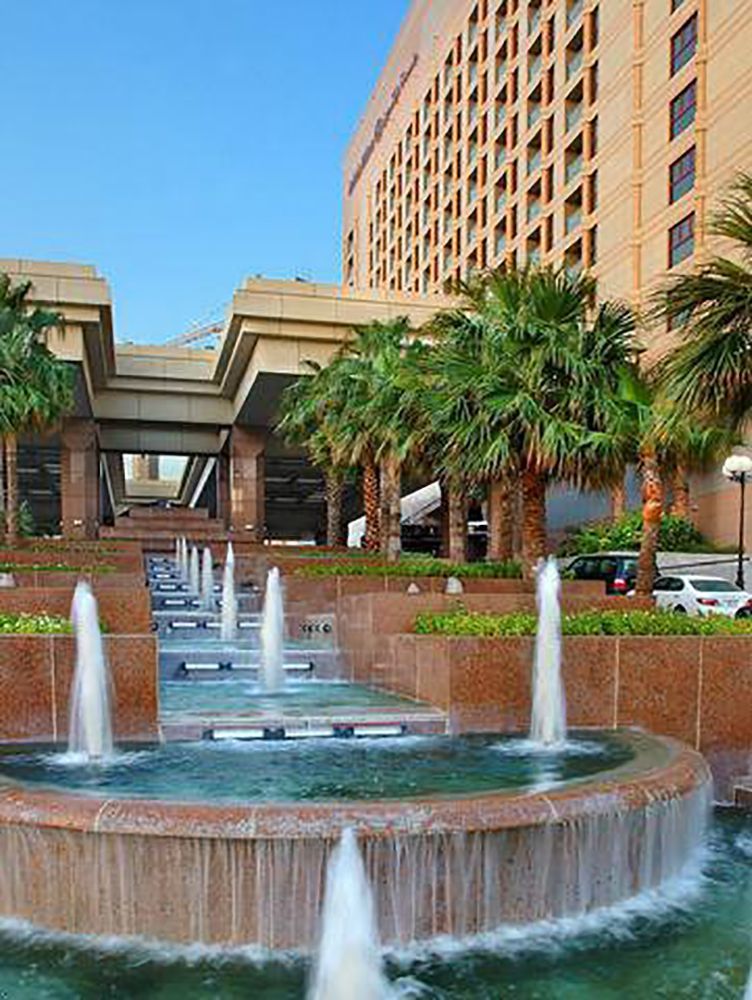 A fountain in front of a large building with palm trees.