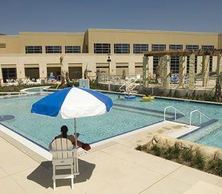 A man sits under an umbrella near a swimming pool