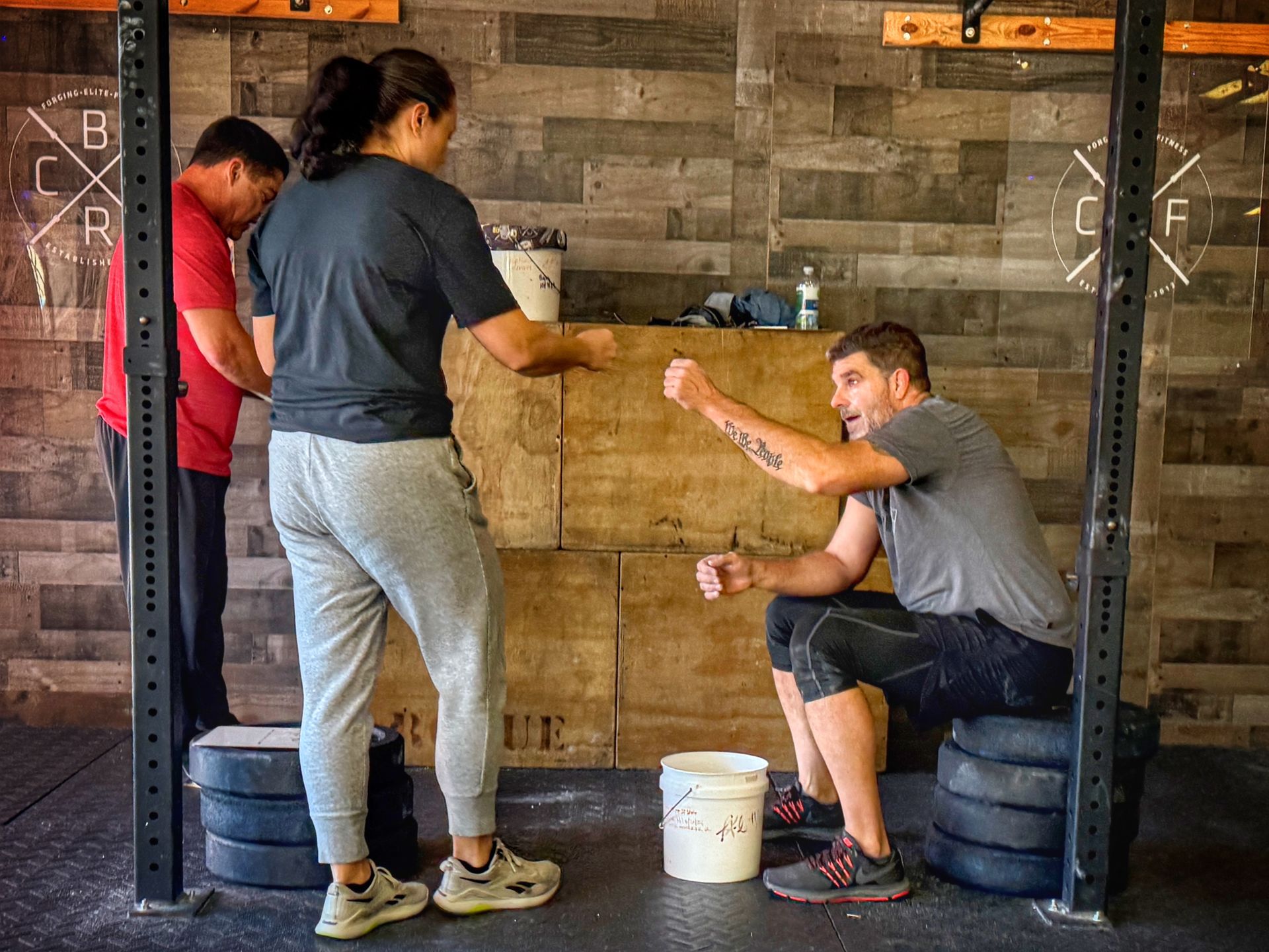 People at CrossFit Boiler Room gym  in Villa Rica, GA, one seated, gesturing. Others are standing by equipment.