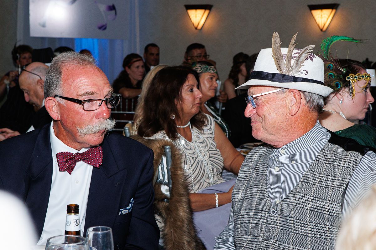 Two men are sitting at a table talking to each other at a party.