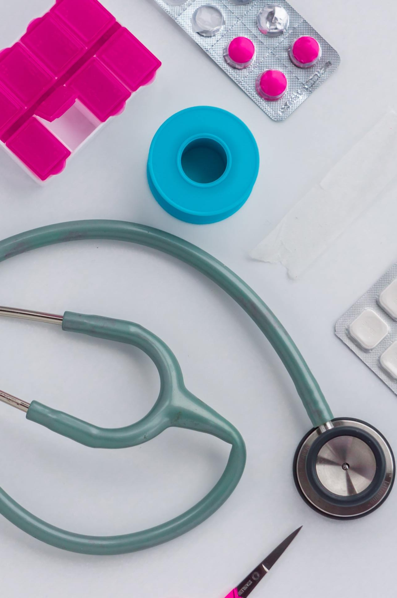 Stethoscope, pills, tape, and pill organizer on a white surface, suggesting medical care.
