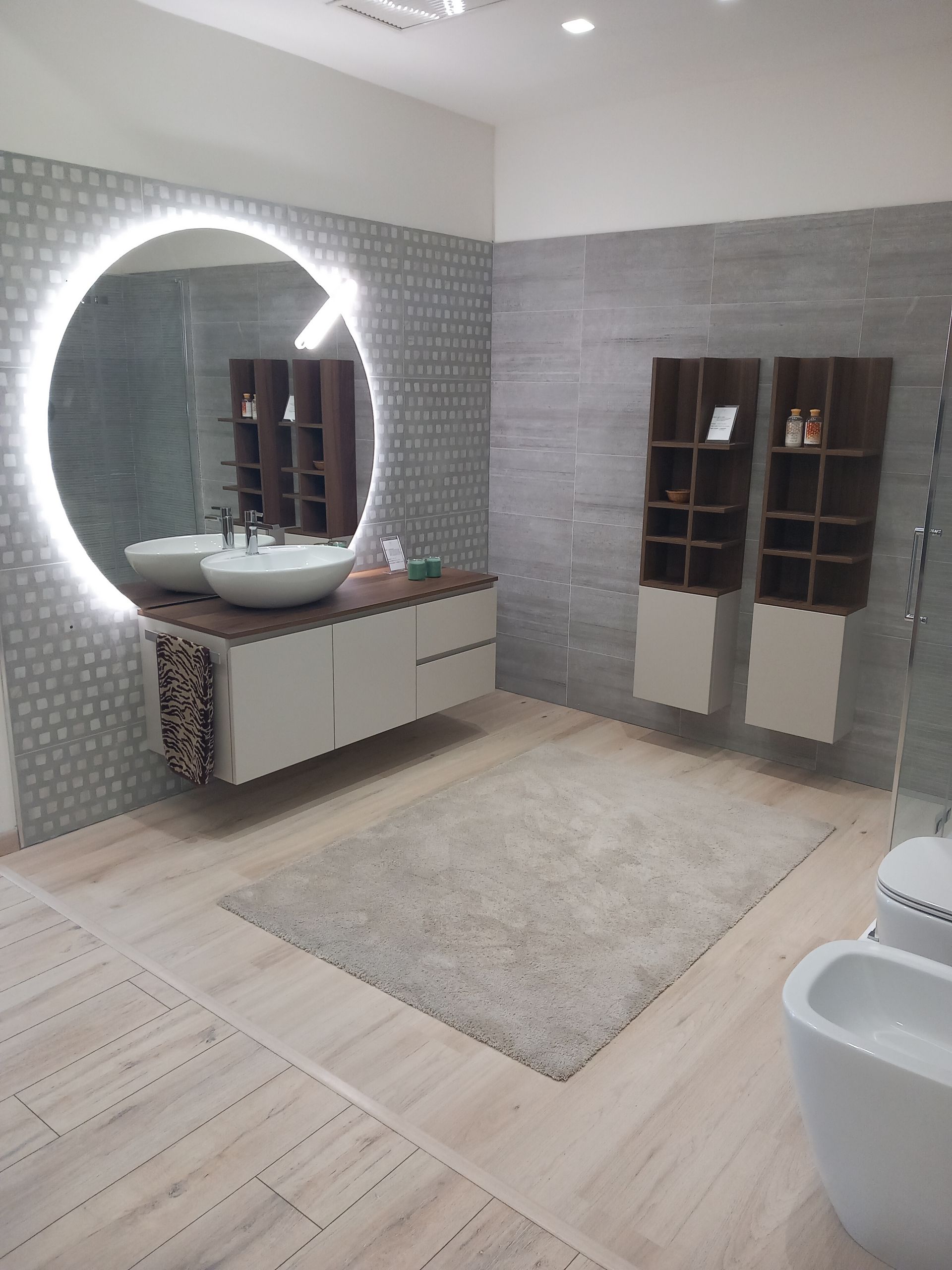 Un bagno con due lavandini, un water e uno specchio rotondo