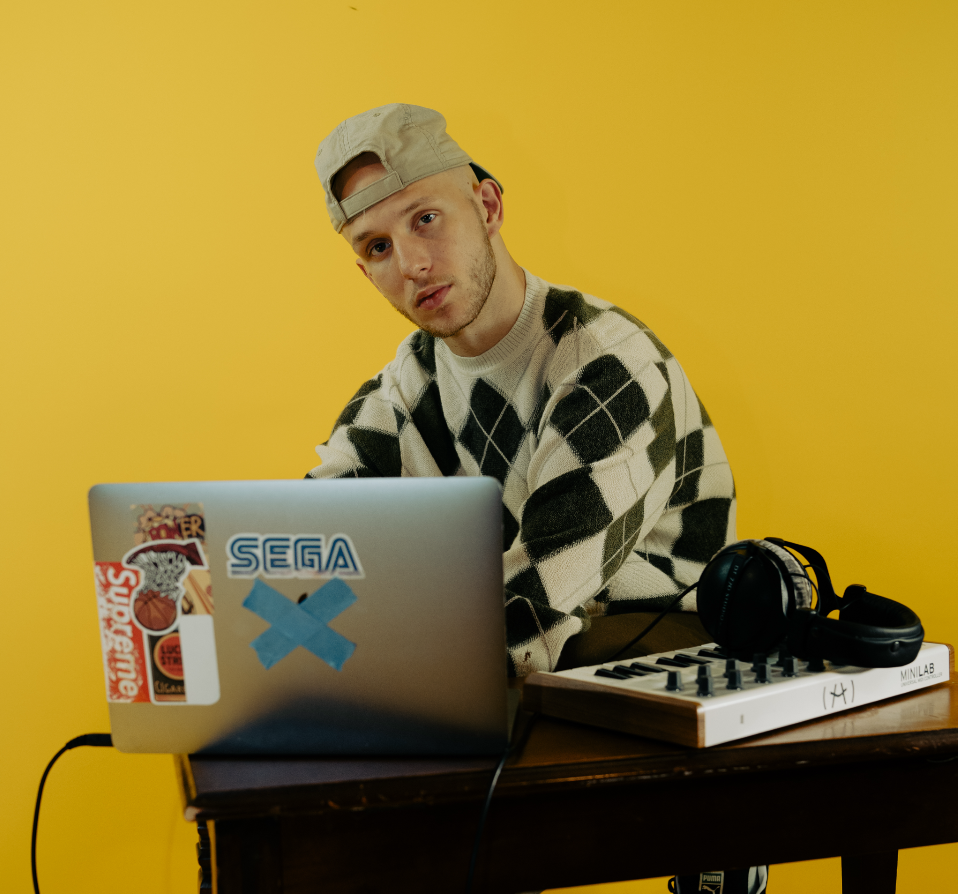 Person at a desk with a laptop and audio gear against a bright yellow background