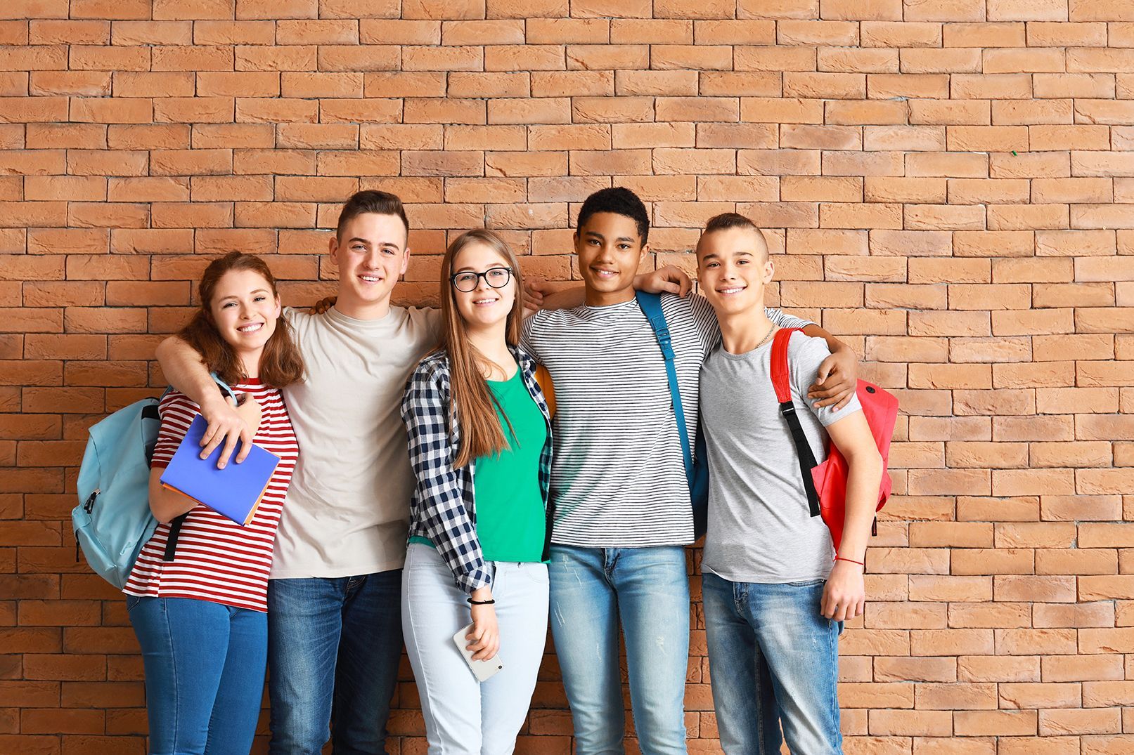 A group of young students are posing for a picture in front of a brick wall.