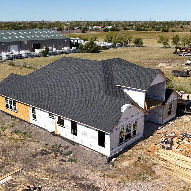 Aerial view of a partially built white house with a dark roof on a construction site.