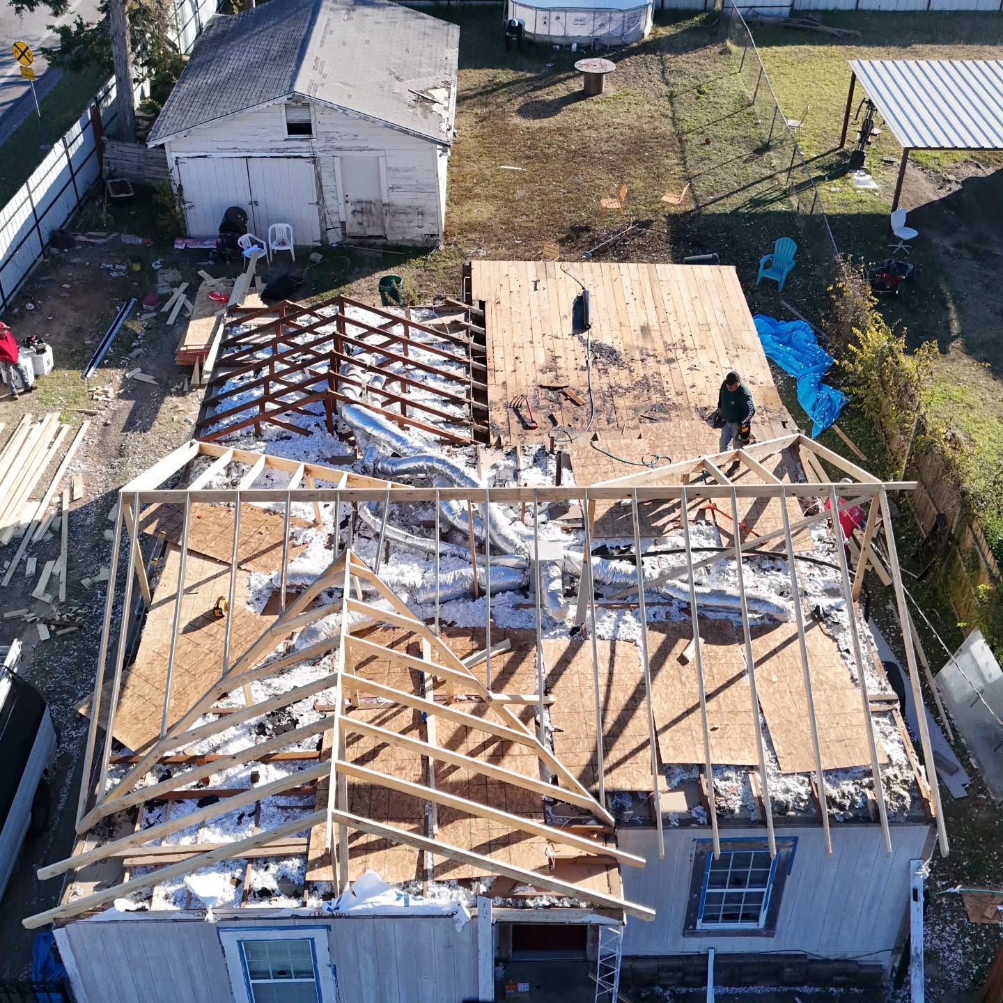 Aerial view of a house roof under repair, with exposed rafters and plywood decking.