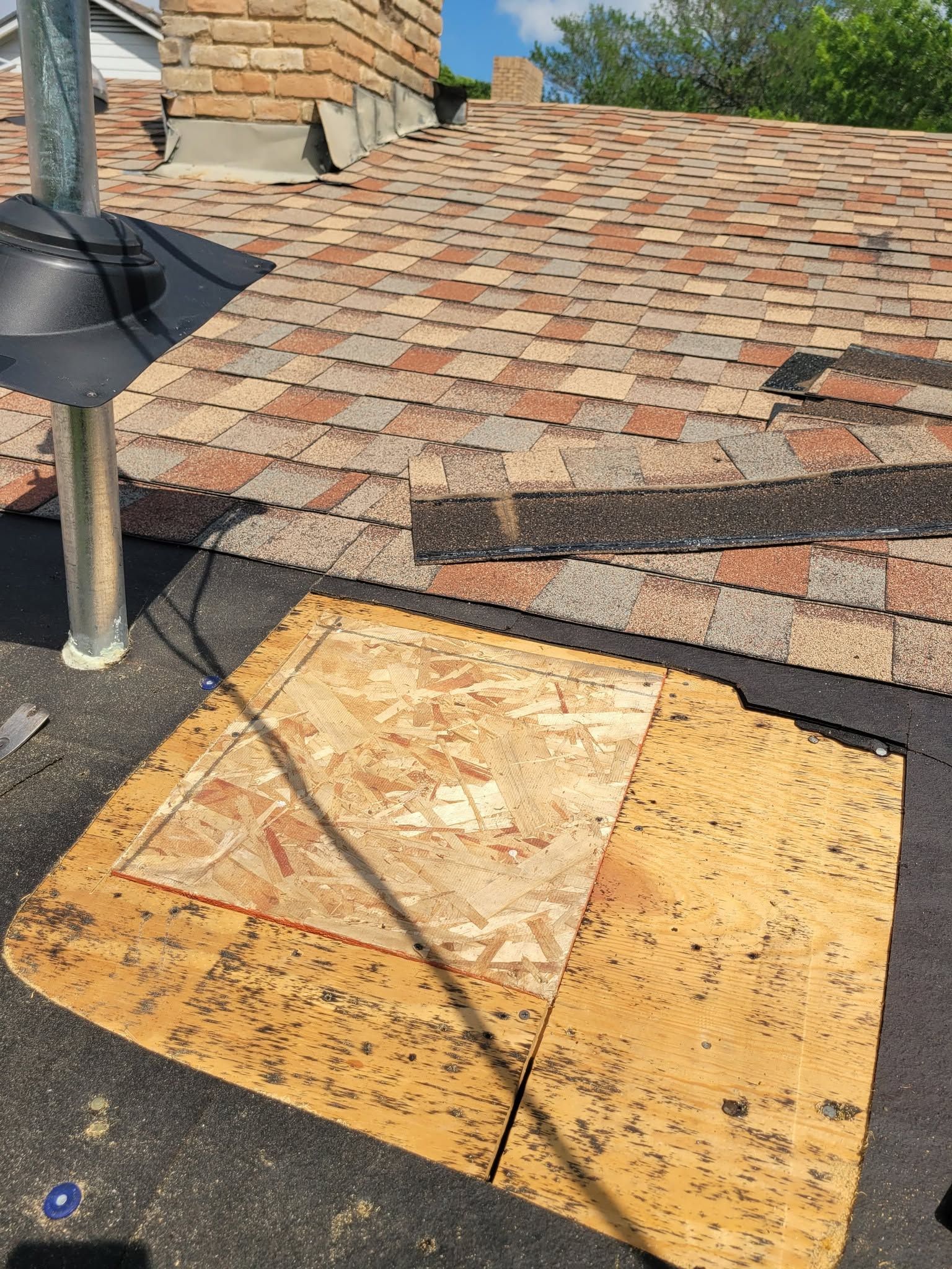 Roof under repair with exposed plywood and shingles, and a safety anchor near the chimney.