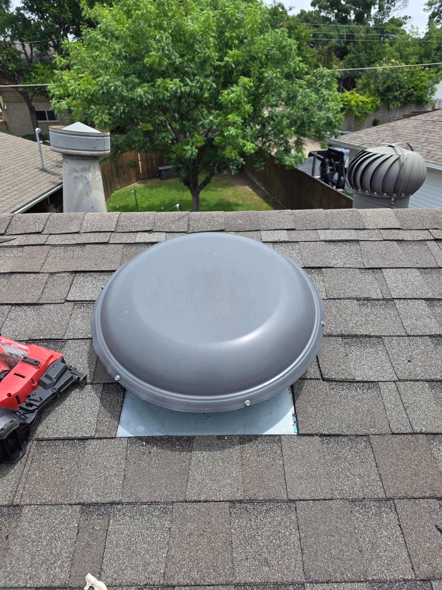 Gray roof vent on a shingled rooftop with trees and neighboring roofs in the background