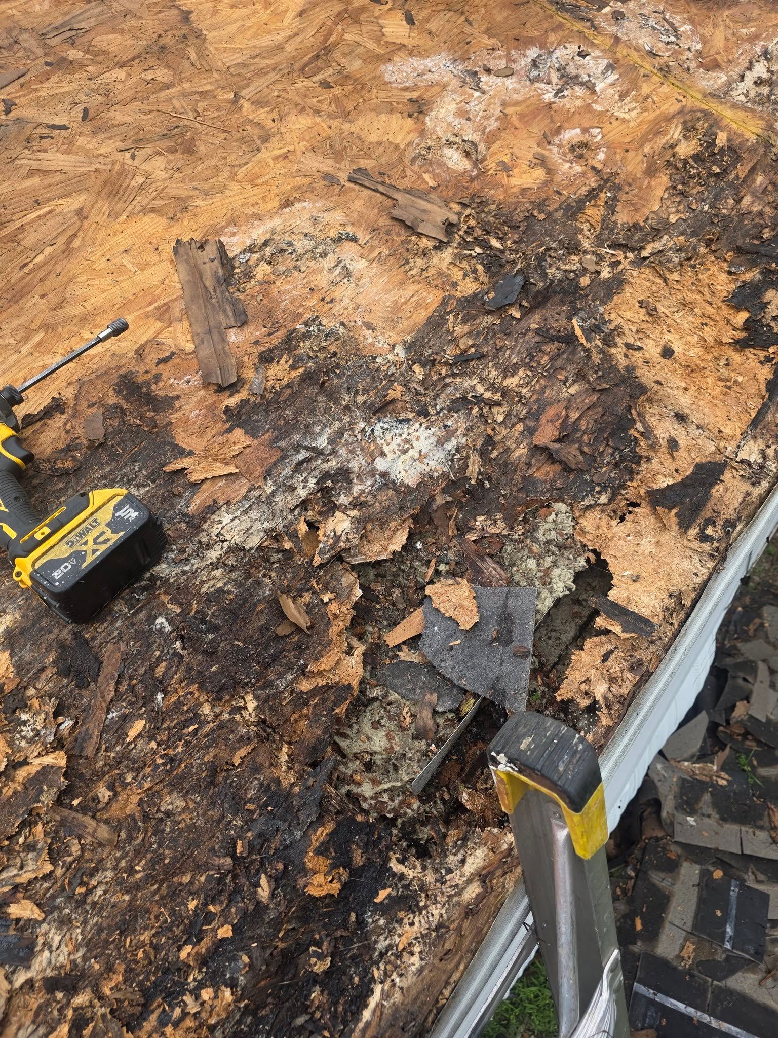 Damaged roof with charred sections and debris near the edge, with a tape measure on the left.