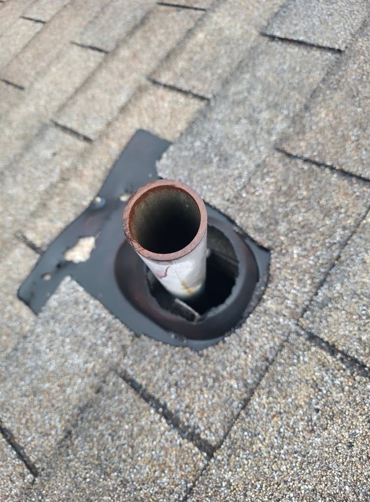 Roof vent pipe with black flashing on gray asphalt shingles.