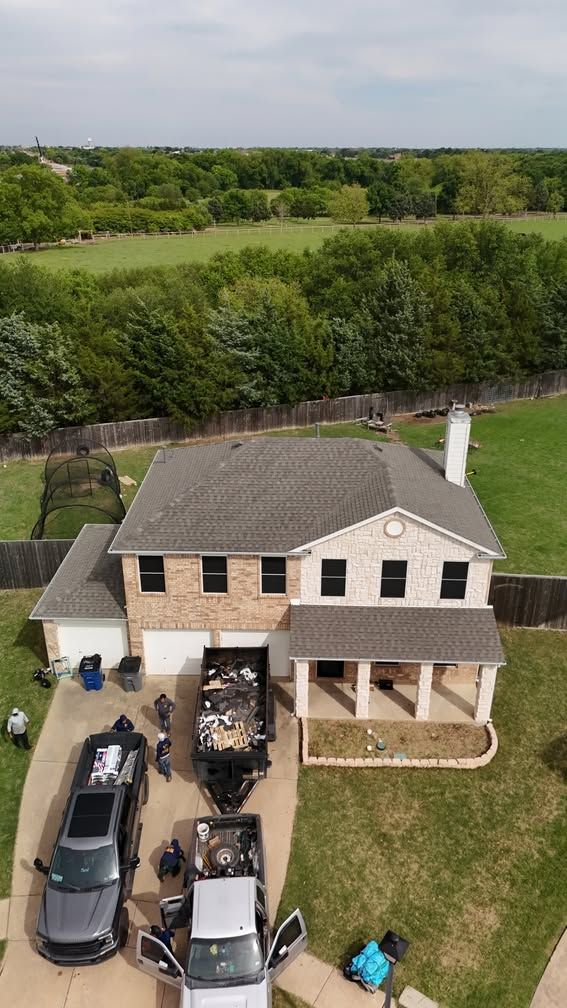 Aerial view of a beige two-story house with several vehicles parked in the driveway and a green backyard.