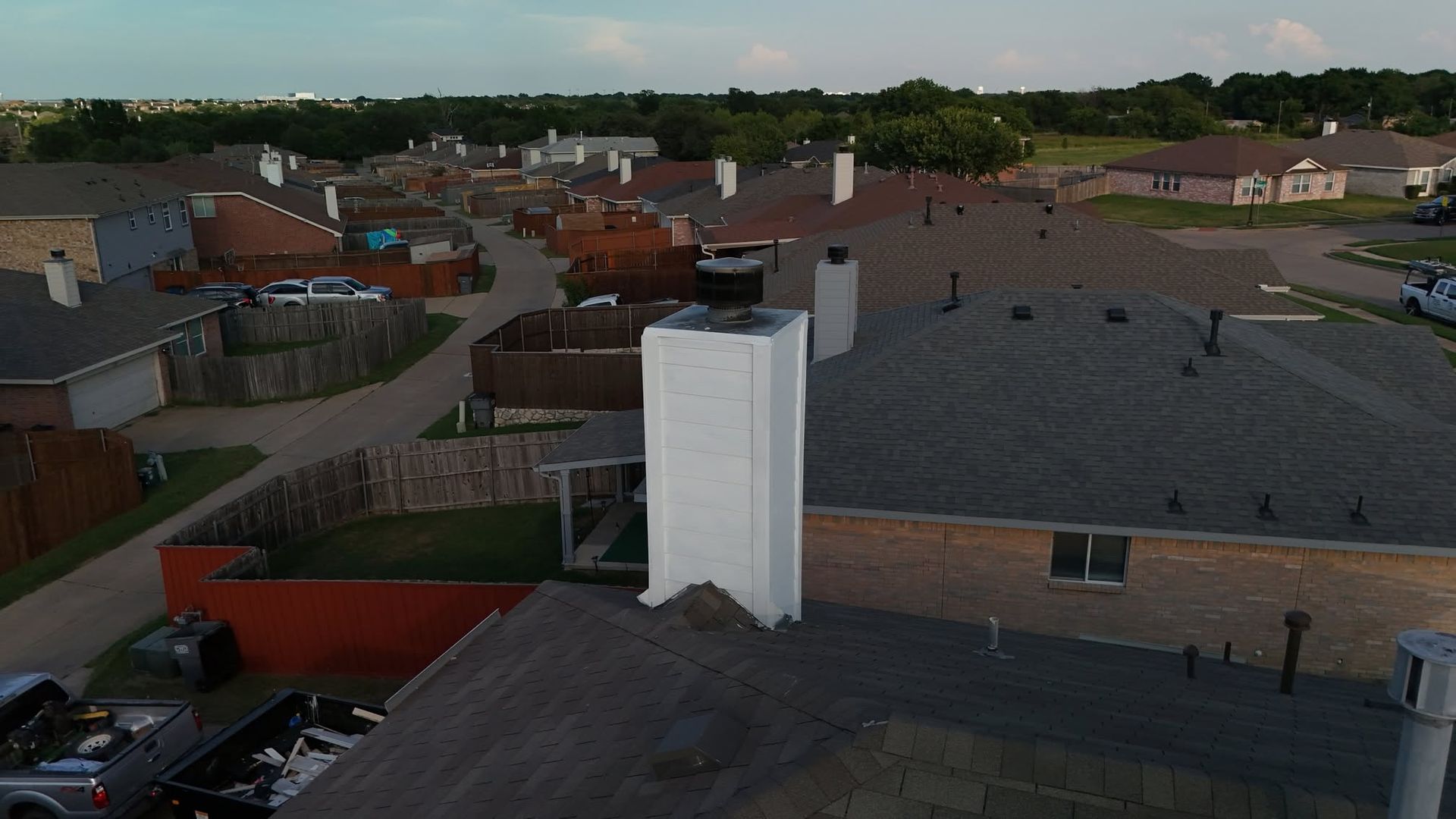 Aerial view of suburban houses with red and gray roofs and a tall white chimney in the foreground.