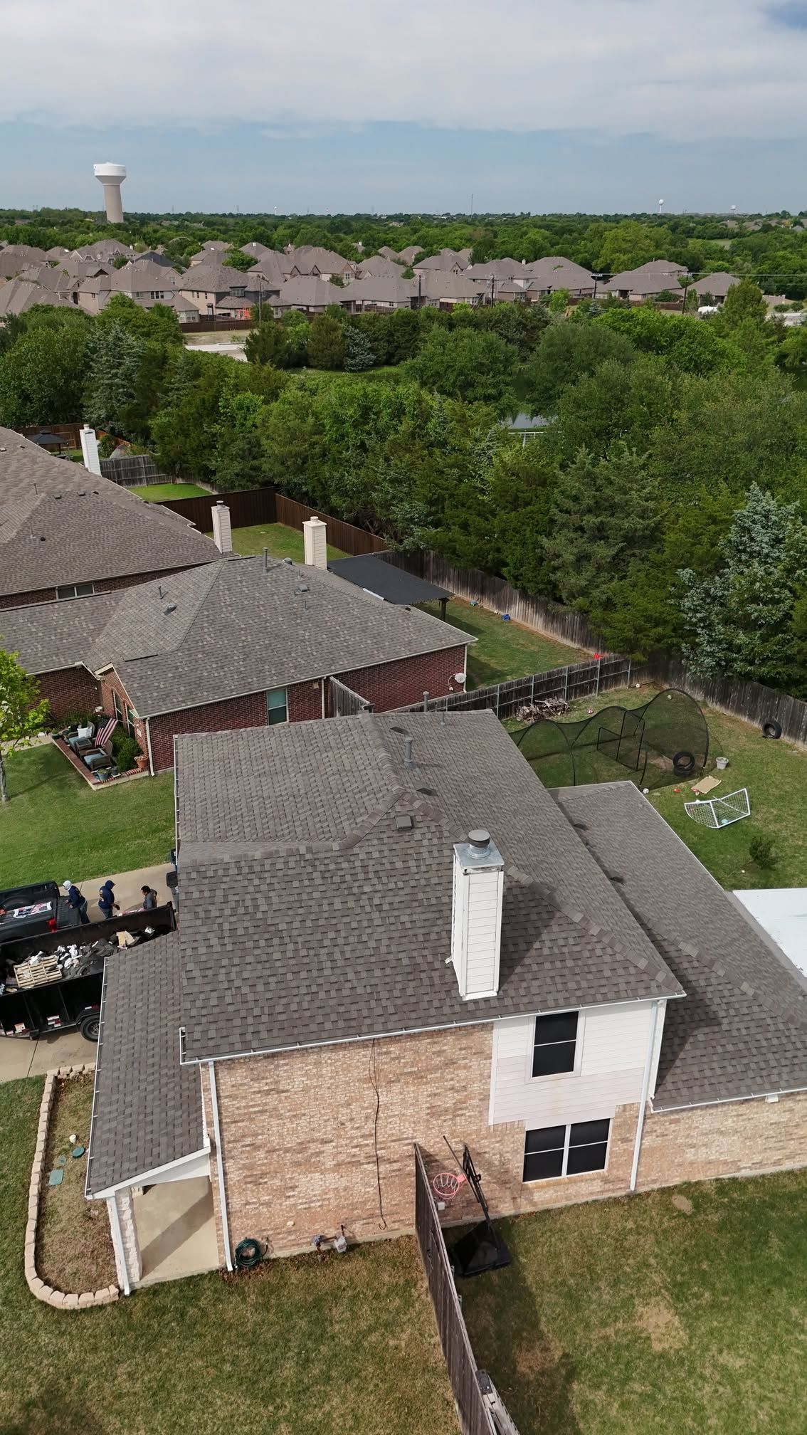 Aerial view of suburban homes with gray roofs, green yards, and trees under a clear sky