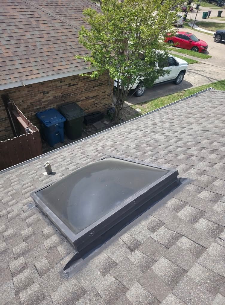 Flat rooftop with a skylight, shingle roofing, and a street with parked cars below.