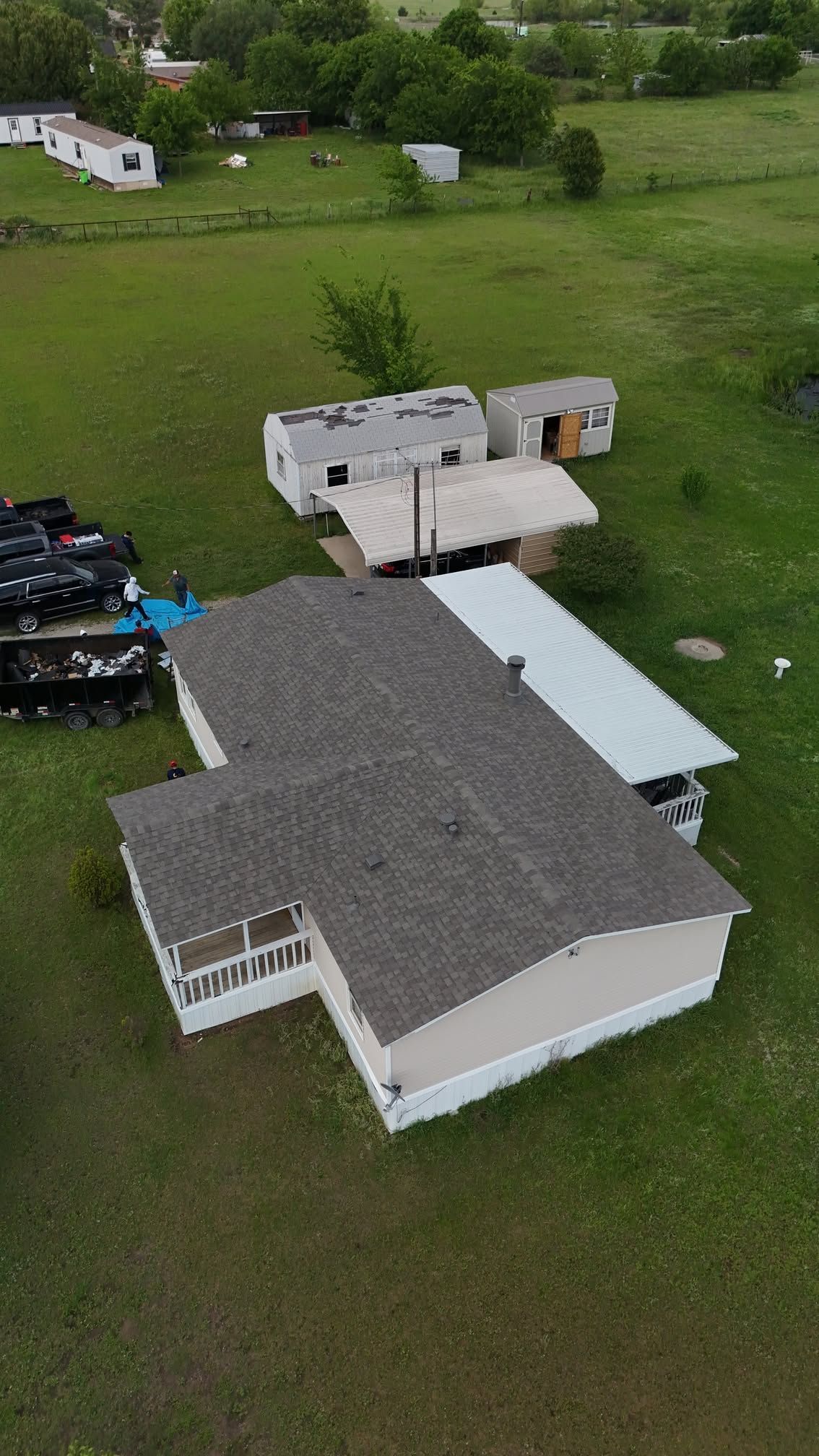 Aerial view of a white house with gray roof, an RV, and a truck parked on a grassy rural property.