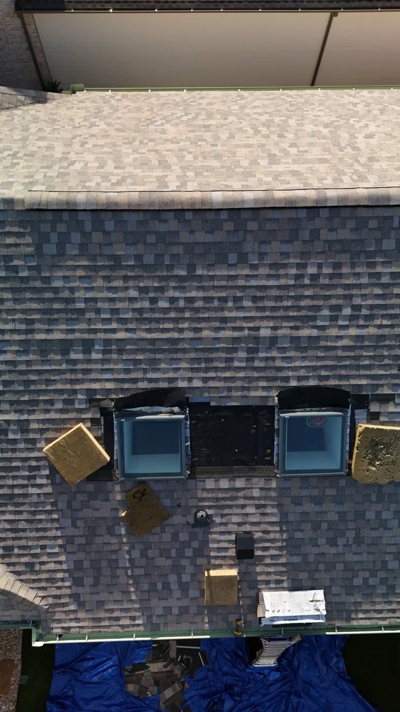 Aerial view of a building roof with dark shingles, two skylights, and small wall-mounted units.