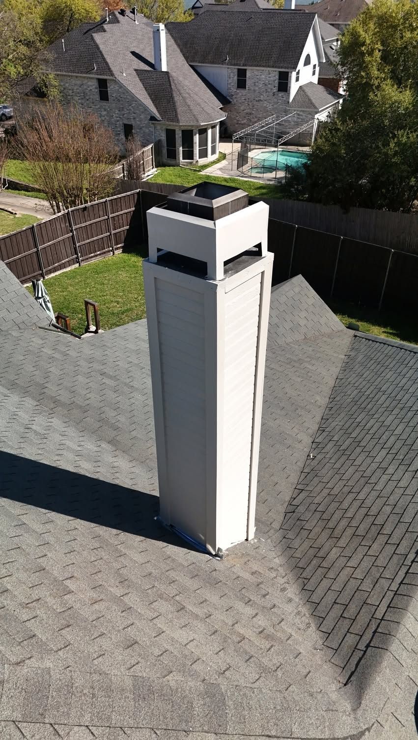 Tall white rooftop chimney on a gray shingle roof in a suburban neighborhood.