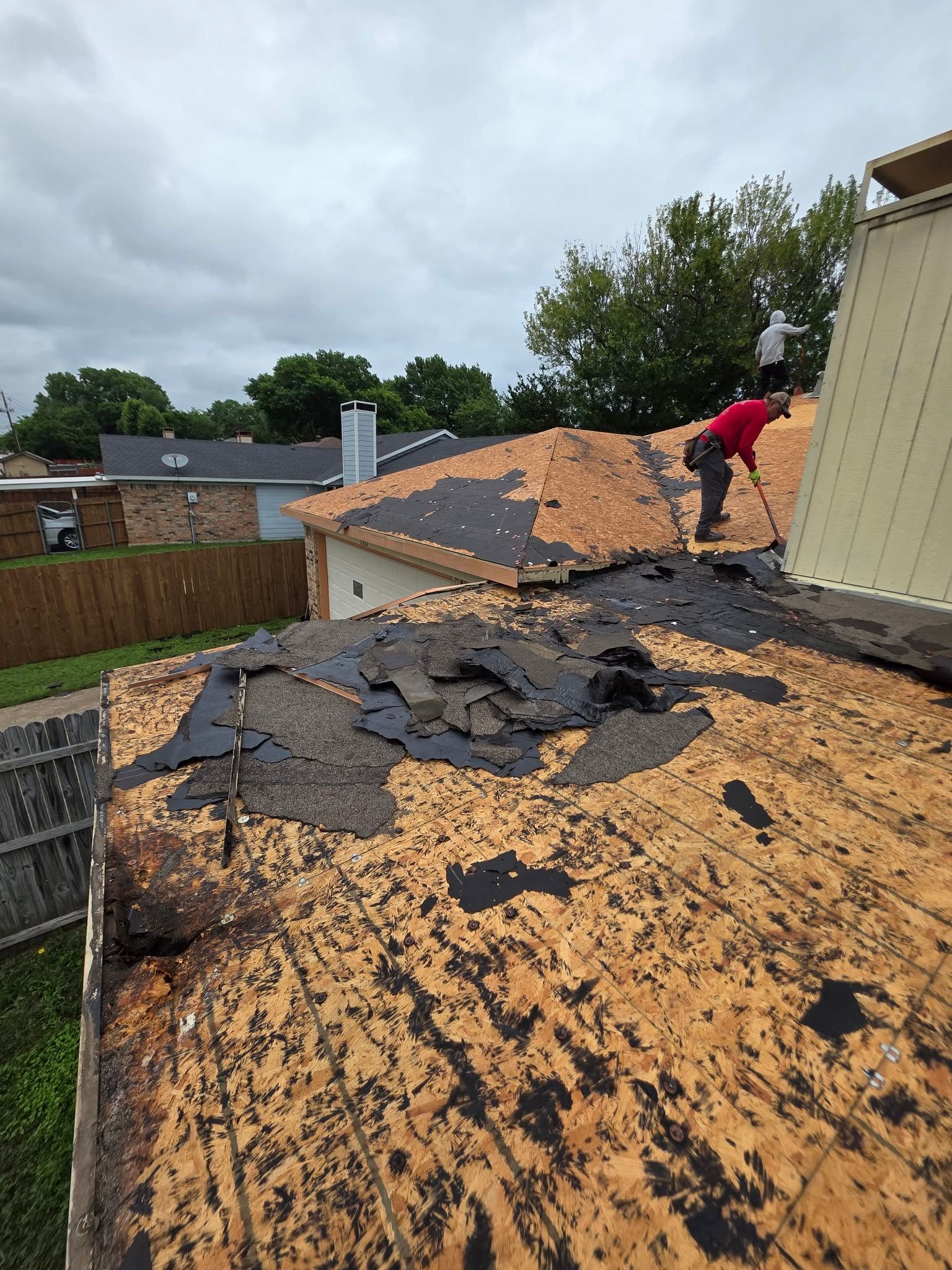 Roofing worker removing old shingles on a damaged roof under cloudy skies