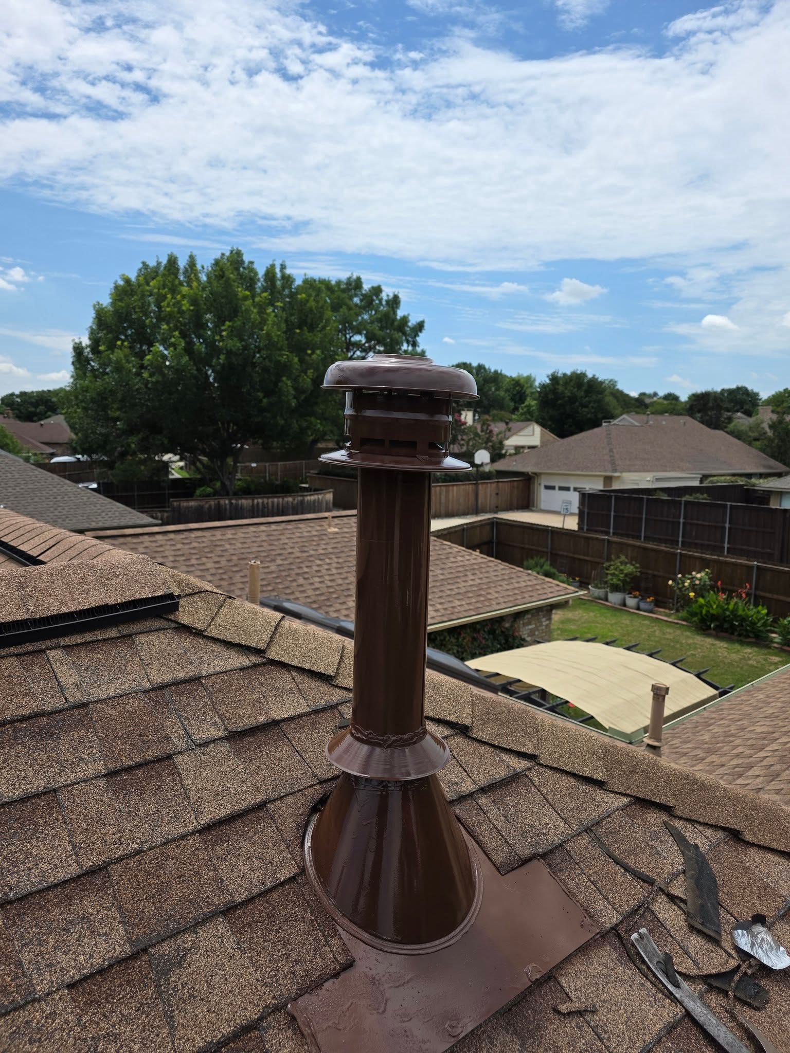 Rooftop metal chimney vent on brown shingle roof under a bright blue sky