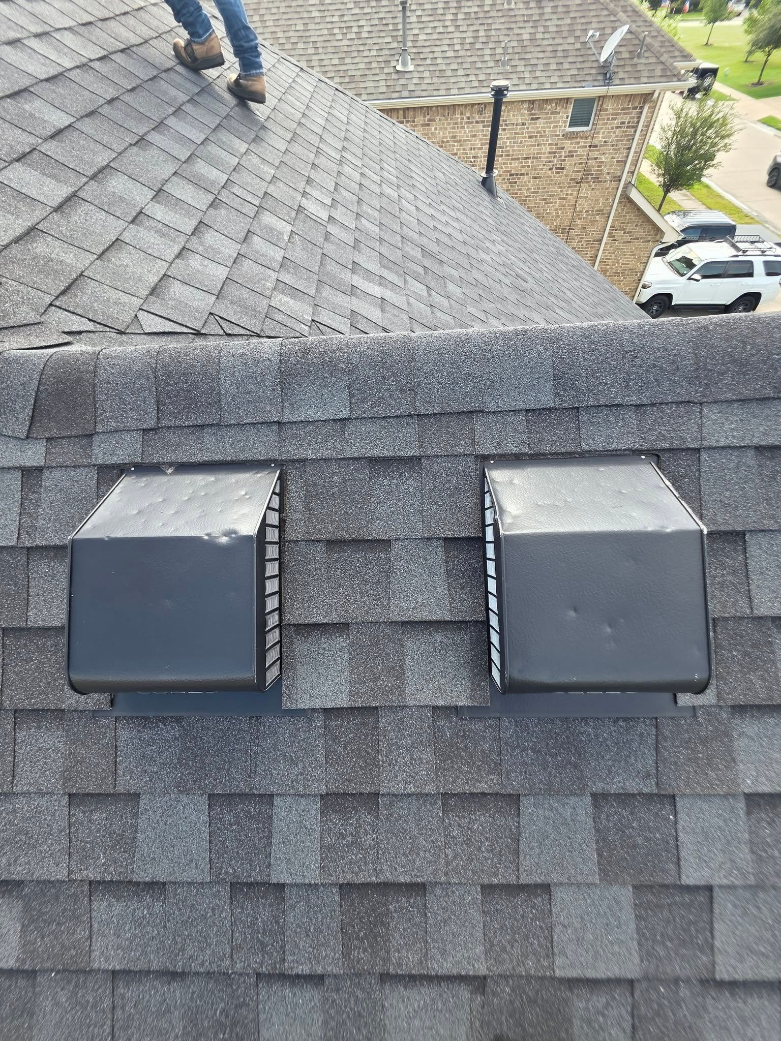 Roof with two gray vent boxes and a ridge cap on dark shingles