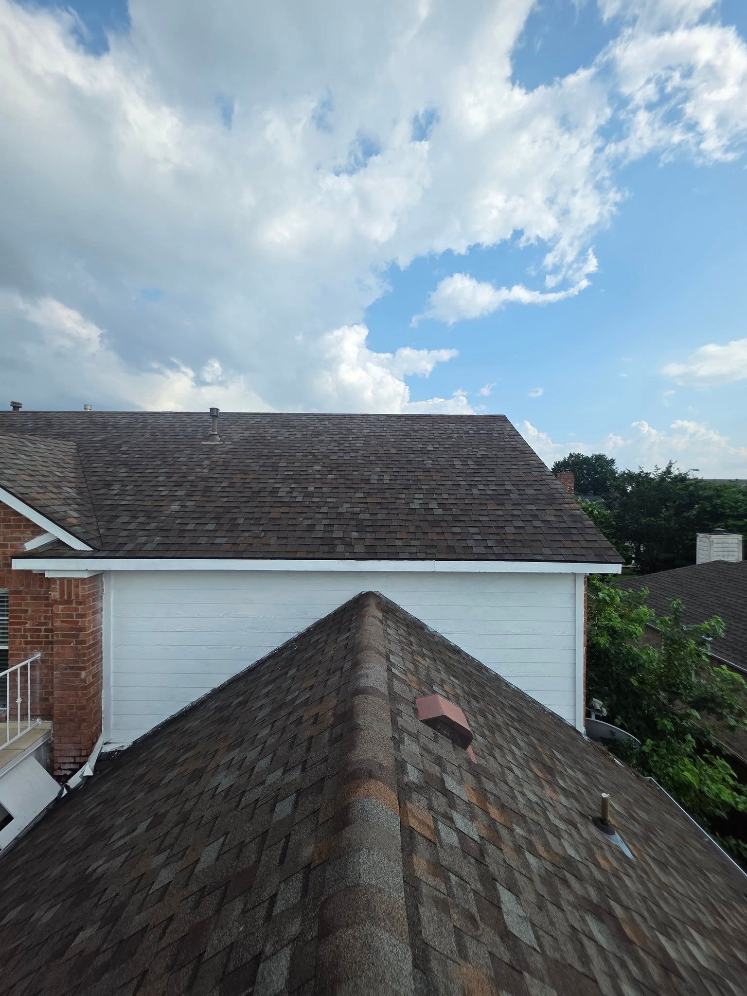 Rooftops with weathered shingles and a white wall under a partly cloudy blue sky