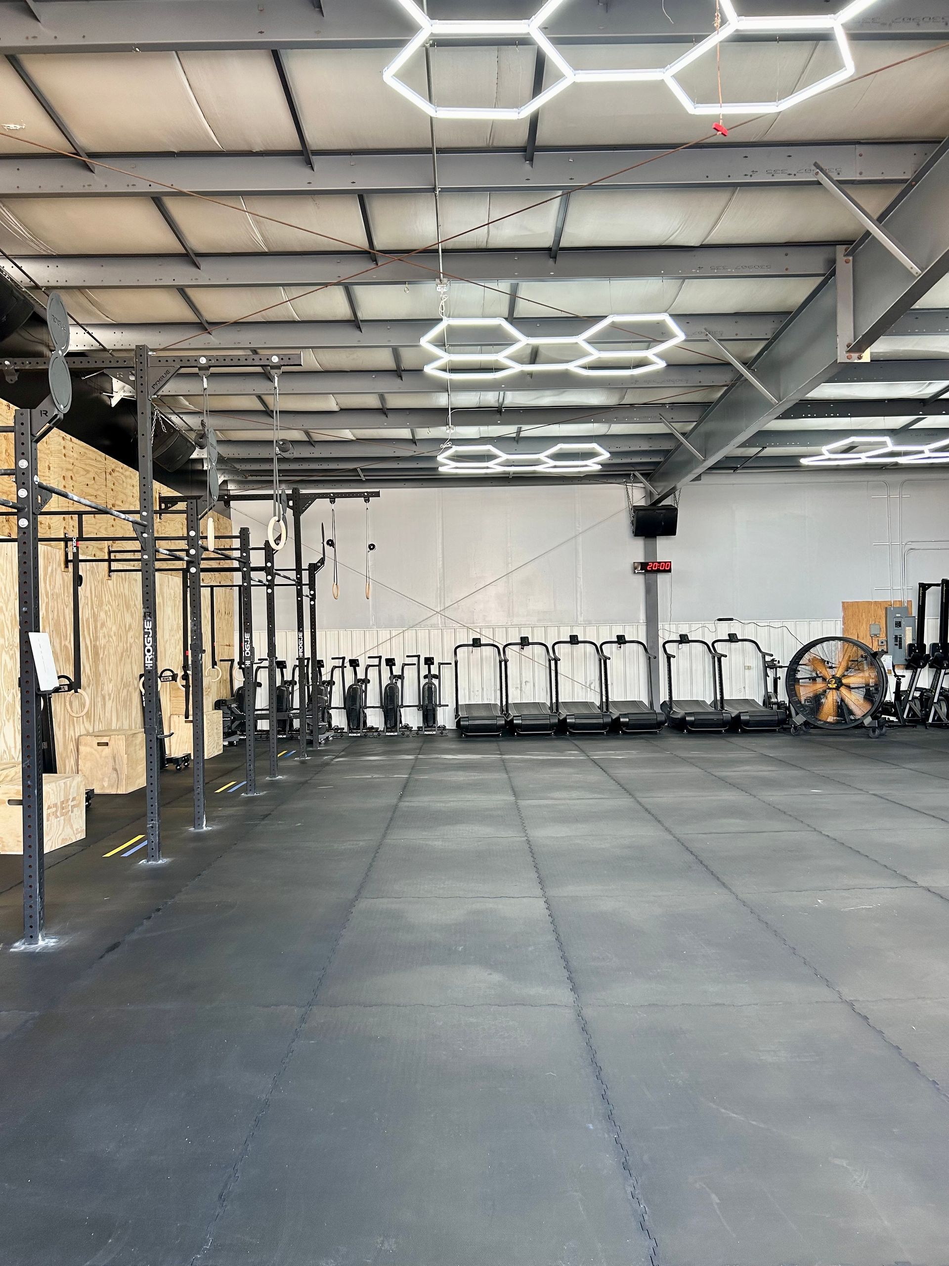 Empty Gray Duck CrossFit gym in Mankato, MN with black floor mats, hanging hex lights, and cardio machines along the back wall.