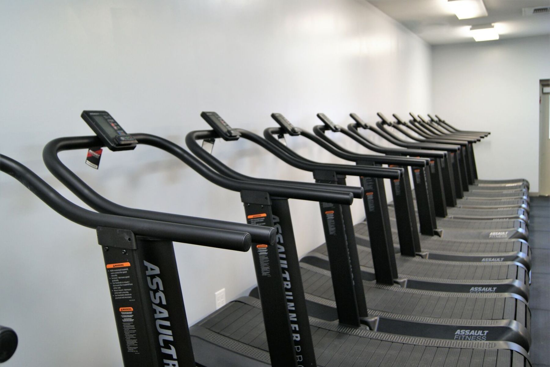 Row of black treadmills lined up in Gray Duck CrossFit gym in Mankato, MN against a white wall