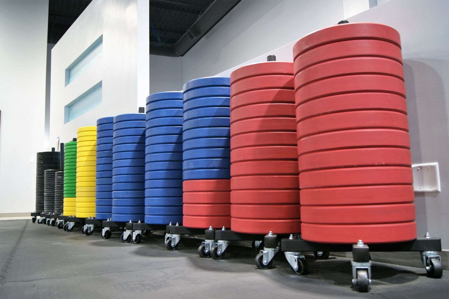 Rows of colorful stacked wheeled bins in an indoor storage area of Gray Duck CrossFit gym in Mankato, MN, arranged by color from green to red.