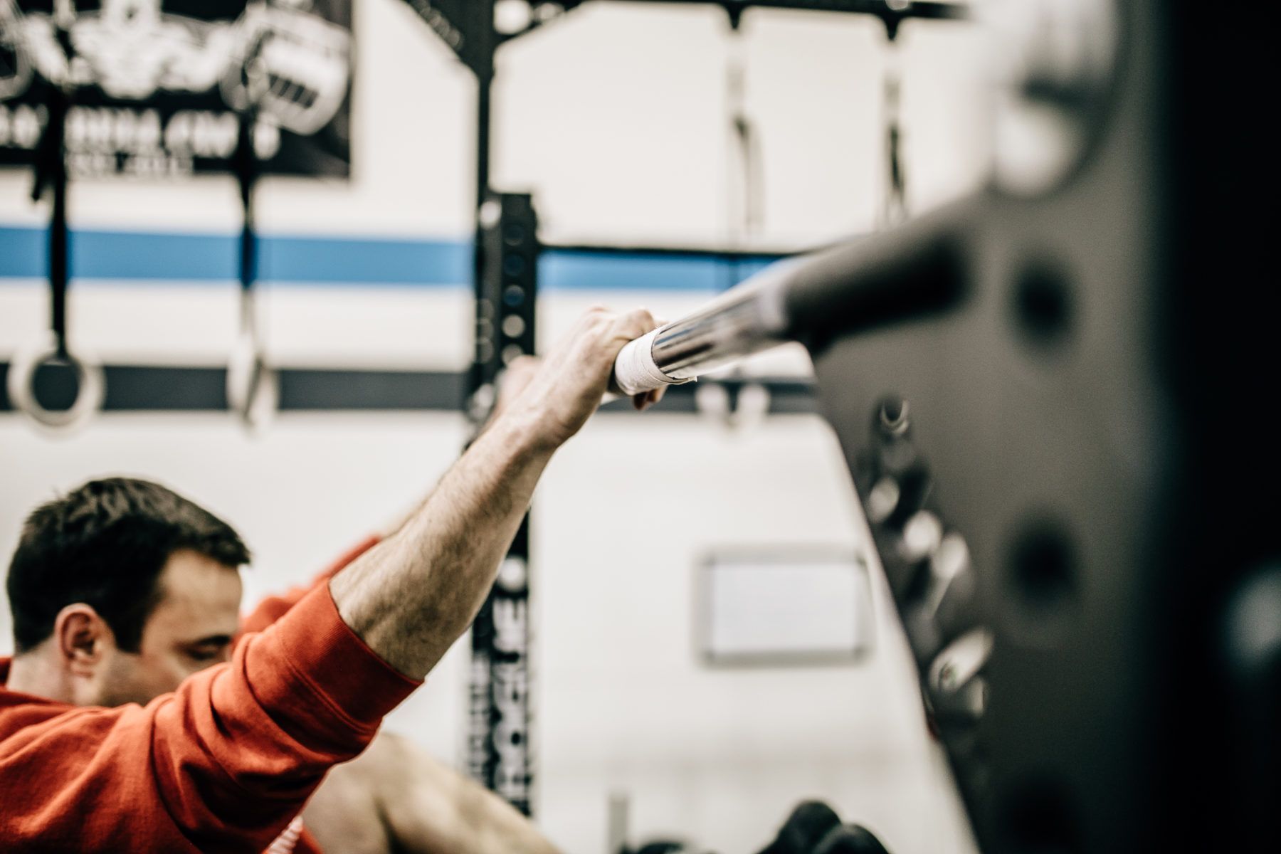 Person reaching up to grip a bar in a gym with weight equipment in the background