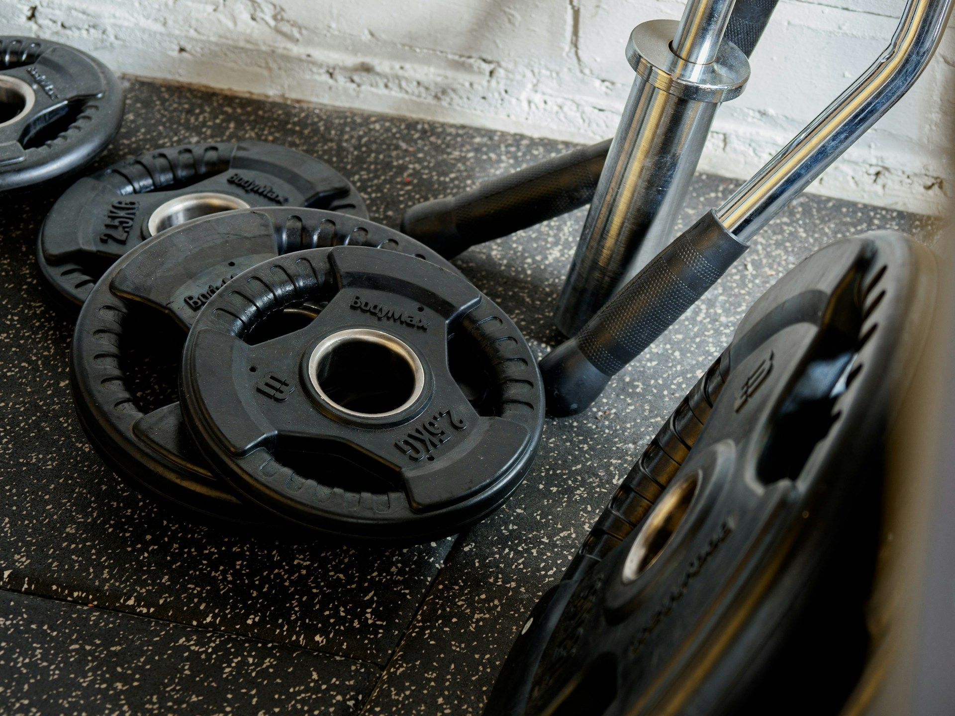 Black weight plates loaded on a barbell in a gym rack, with a chrome bar and textured floor.