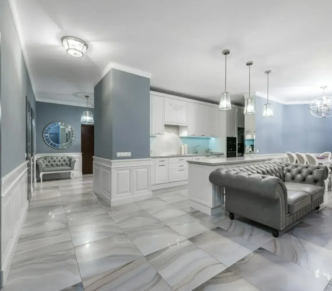 Bright open-plan kitchen and living room with gray tufted sofa, white cabinets, and blue accent walls