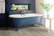 Freestanding blue bathtub in a bright bathroom with a window, potted plant, and side table