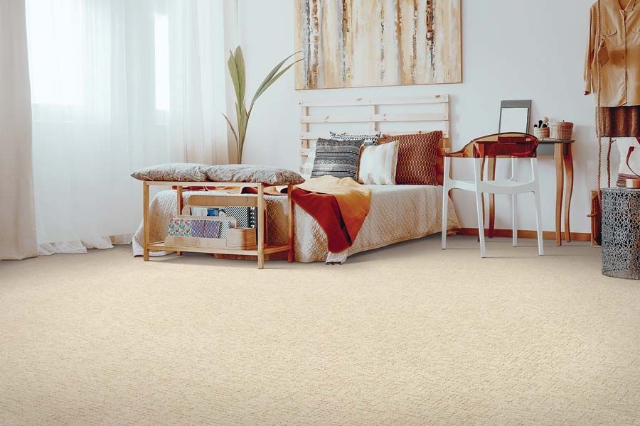 Bright bedroom with bed, white desk, red chair, and cream carpet near sheer curtains