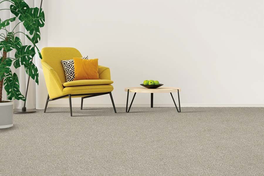 Yellow armchair and small coffee table in a minimalist room with a plant and gray carpet.