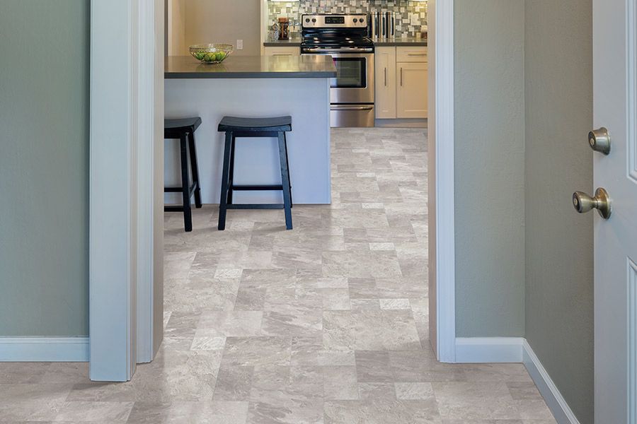 Hallway opening to a bright kitchen with an island and two bar stools, beige tile flooring.