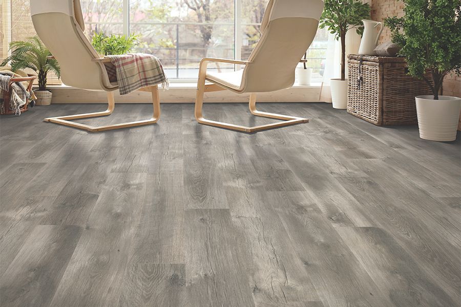 Modern gray wood-look flooring in a bright room with two chairs, a plaid blanket, and potted plants.
